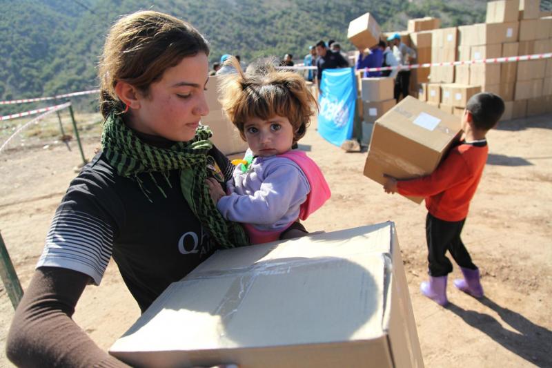 An adolescent girl holds a younger girl in one arm and a box of winter clothes in the other, in Dohuk, in the Kurdistan Region of Iraq.