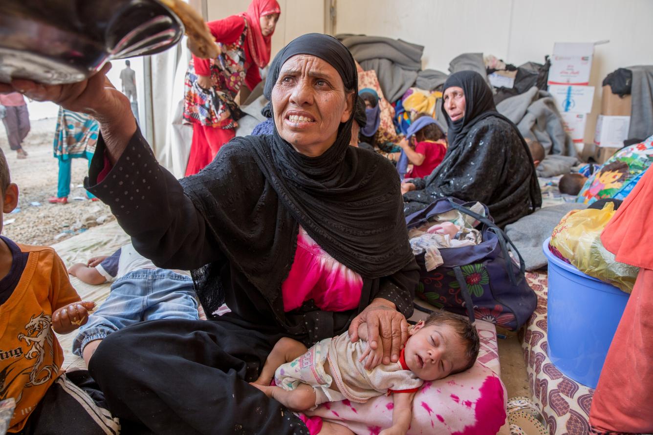 The grandmother of one-month-old Abdallah, reaches for a bowl of food in a temporary shelter.