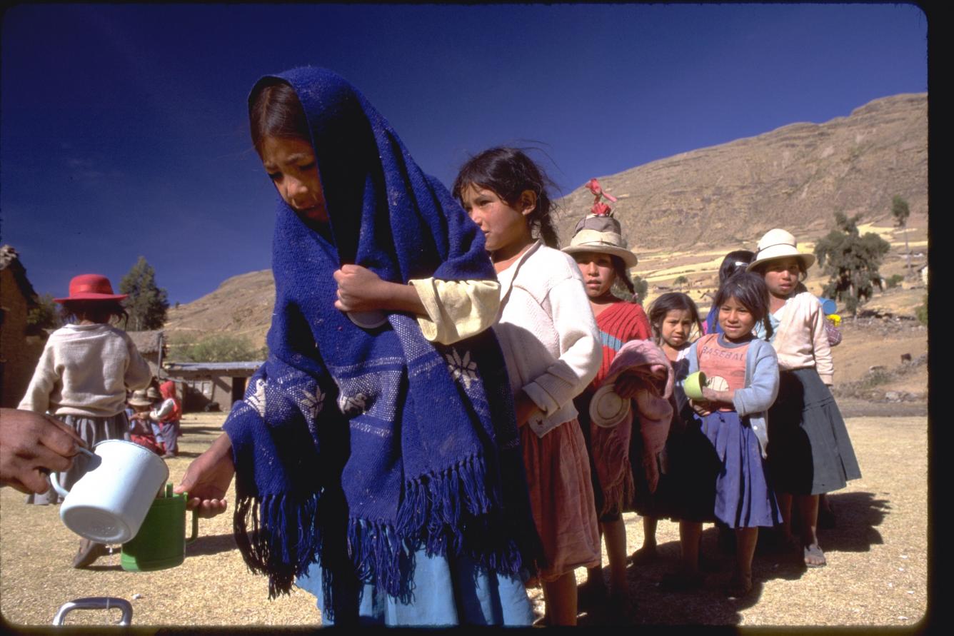 While other children form a line behind her, a girl from the Quechua indigenous group in Bolivia receives fortified milk brought, together with bread, by UNICEF.