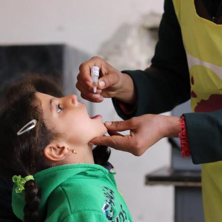 A girl receives an oral polio vaccine dose by a UNICEF worker during an immunization campaign in Aleppo, Syria. 