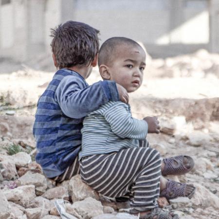 Two children sit in the rubble of their former home.