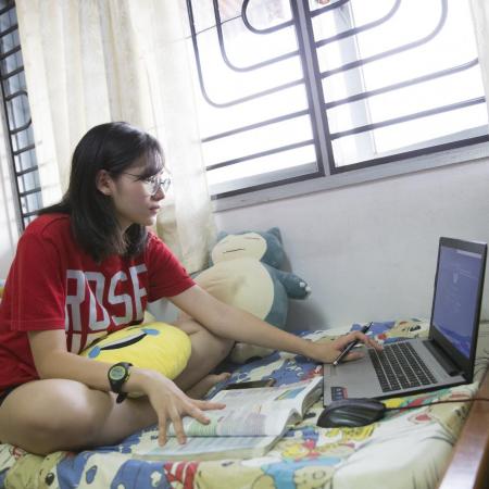 Youth sits on her bed reading laptop screen