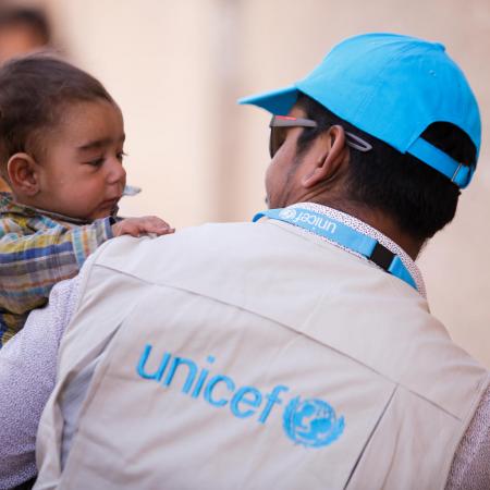 A UNICEF aid worker carries a baby at a supply depot in Syria.