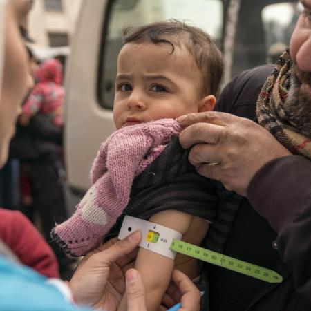 On 10 February 2023, Sondos, two years and eight months, in her father’s arms, is screened for malnutrition by a UNICEF-supported mobile health team worker, using a mid-upper arm circumference (MUAC) tape, in the Alsalheen neighbourhood, Aleppo city, north Syria.