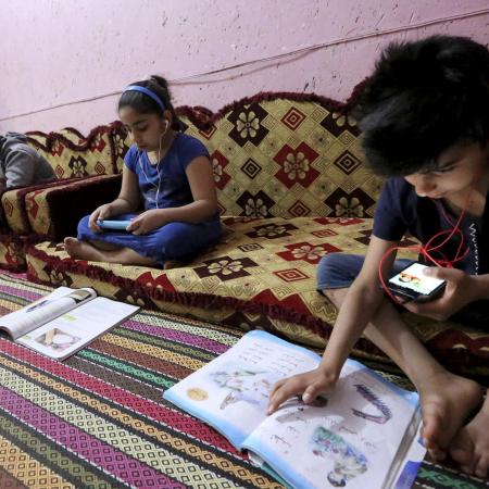 Children study using recorded lessons at a refugee camp.