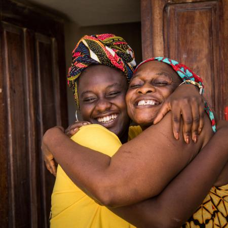 A mother and daughter hug outside their home.