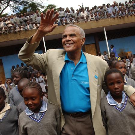 UNICEF Goodwill Ambassador Harry Belafonte waves to onlookers, standing amidst a crowd of children at the Kihumbuini primary school in Kangemi, a poor neighbourhood in Nairobi, the capital.