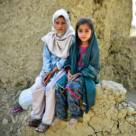 Muriko bibi (7) and Tehseen (6) sit on the damaged wall of their mud house which was almost destroyed during the 2022 floods in Pakistan.