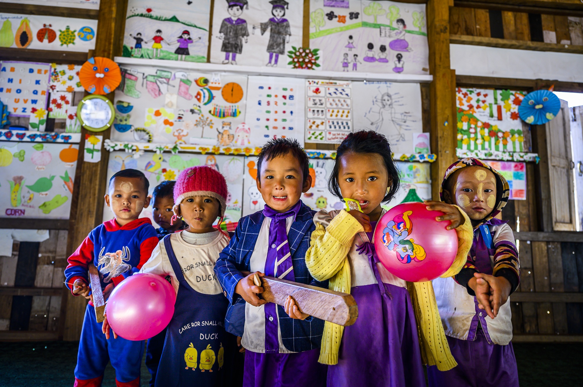 Children hold balloons while they pose for a photo in a classroom.