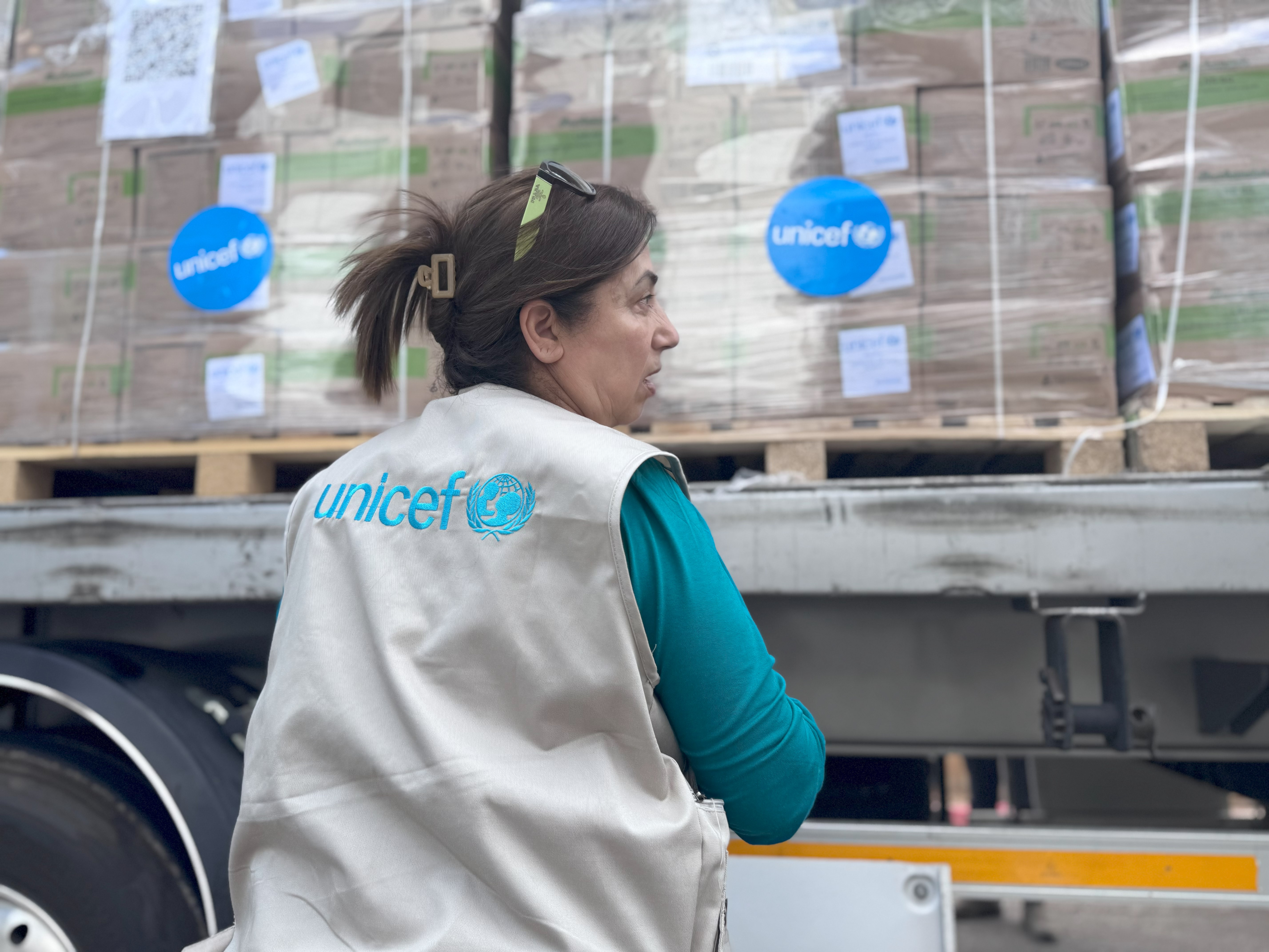 Woman wearing a UNICEF vest standing in front of UNICEF supply truck.