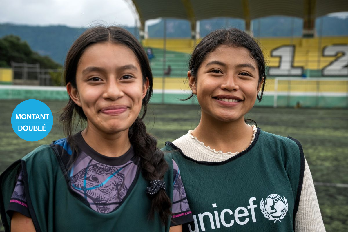 Deux filles souriantes portant des gilets verts de l’UNICEF, debout sur un terrain de sport.
