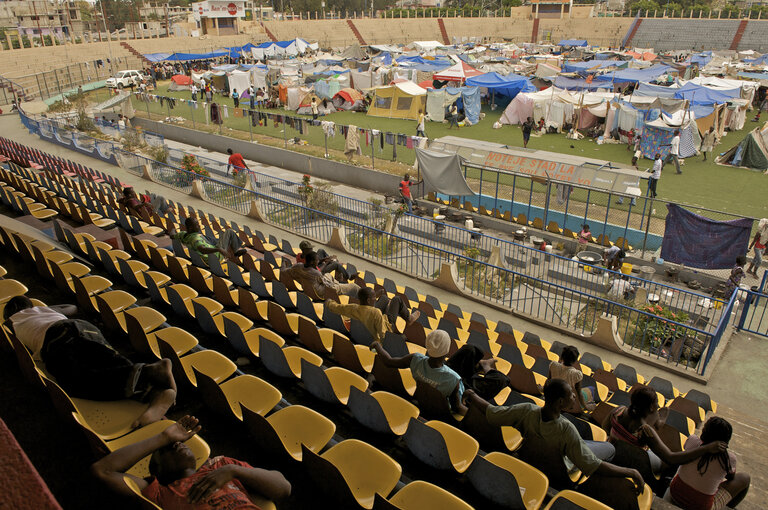 On 1 February, people sit and sleep in a section of the stands at Sylvio Cator Stadium in the centre of Port-au-Prince, the capital. The stadium is serving as a temporary settlement area for some 4,000–6,000 people who have been displaced by the earthquake. It is also the site of the initial pilot vaccination round of an immunization campaign aimed at up to 500,000 children under age seven who have been affected by the disaster. An immunization tent is visible at far left. 