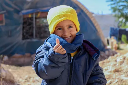 In Syria, 4-year-old Rashid smiles and gives a thumbs-up sign, while wearing his new winter clothes distributed by UNICEF in Fafin camp for displaced families.