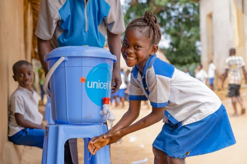 In the Democratic Republic of the Congo, a girl smiles at the camera while washing her hands. 
