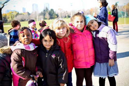 A diverse group of children stand shoulder to shoulder outside on a chilly but sunny day, smiling at the camera.