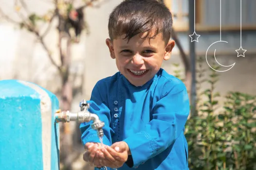 A young boy washing his hands while smiling at the camera.