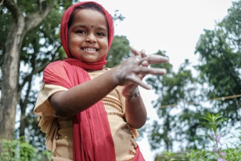 A young girl smiles at the camera while washing her hands with soap. 