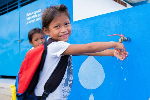 A girl smiles at the camera while washing her hands at a UNICEF tap.