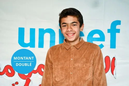 Photo d’un adolescent souriant à l’objectif et se tenant devant une bannière de l’UNICEF.