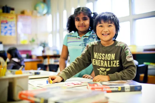 A boy and girl child from diverse backgrounds work together on a project in their school classroom.
