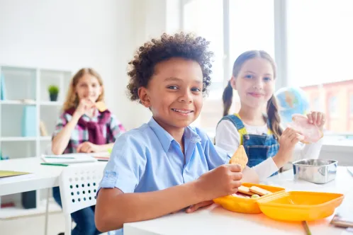 Three children in a classroom eating lunch at their desks.
