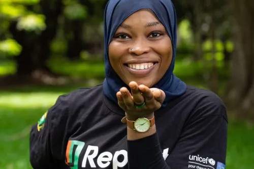 Une jeune fille portant un hijab et un t-shirt U-report sourit en se tenant à l’extérieur.