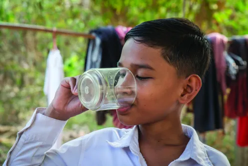 A boy drinks water from a cup.  