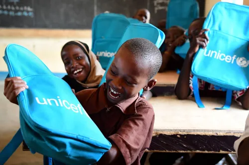 Au Niger, des élèves enthousiastes sourient et rient à leur pupitre après avoir reçu des sacs à dos de l’UNICEF remplis de fournitures scolaires.