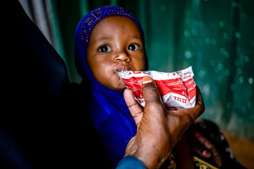 A small child being held by her mother eats from a packet of ready-to-use-therapeutic food.