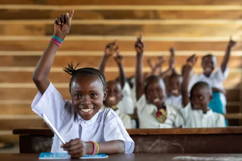 In the Democratic Republic of the Congo, students seated at classroom desks enthusiastically raise their hands during a lesson at their UNICEF-supported school in Goma.
