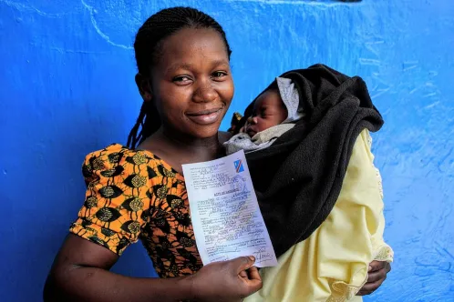 A smiling mother holds her baby and a certificate of birth registration, in Democratic Republic of the Congo.