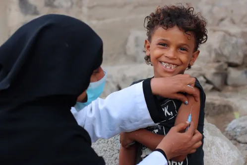 Young child smiling at the camera while getting vaccinated in Yemen.