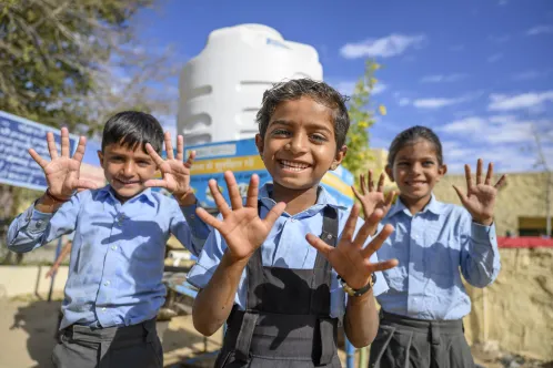 Three school children showing their washed hands  smile at the camera. 