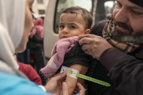 A baby in her father’s arms, being screened for malnutrition by a UNICEF-supported mobile health team worker, using a mid-upper arm circumference (MUAC) tape.