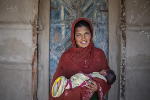 Une femme tient un bébé dans ses bras et sourit à la caméra.
