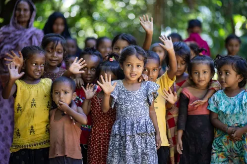 Children standing in a group while waving and looking at the camera.