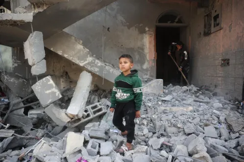 A young boy walks through rubble, surrounded by destruction and debris.