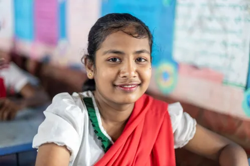Portrait d’une adolescente assise dans une salle de classe et souriant à l’objectif.
