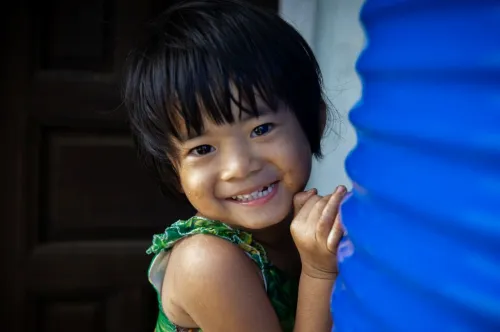 Close-up portrait of a young child smiling at the camera and standing beside a blue water tank.