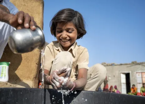 A community member helps a child wash her hands with soap in Bangladesh.