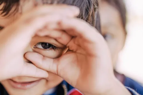 A boy looking through his fingers as if peering through binoculars.  