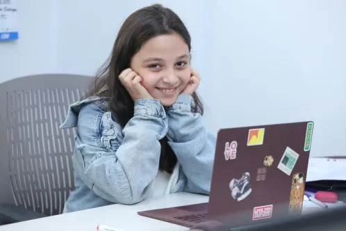 Eva, 12-years-old, sits at her desk while working on a math game on her laptop. 
