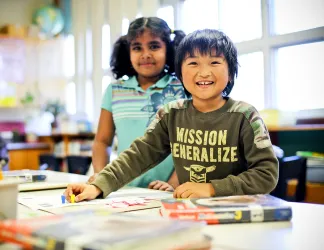 A boy and girl child from diverse backgrounds work together on a project in their school classroom.
