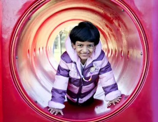 A young girl child is pictured in a red tunnel on a playground. 