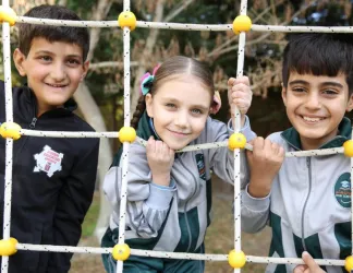 Trois enfants souriants se tiennent ensemble sur un terrain de jeu au Liban.