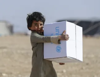 Boy carrying a large UNICEF supply box in his arms.