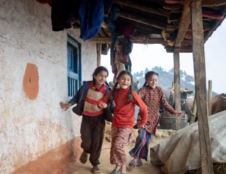 Three girls running and playing beside a house.