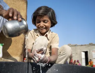 A community member helps a child wash her hands with soap in Bangladesh.