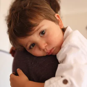 Young child resting their head on a caregiver's shoulder, looking at the camera.