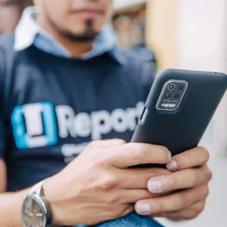 An teenage boy wearing a U-Report t-shirt types on his smartphone. 
